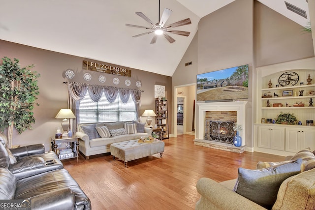 living room featuring ceiling fan, hardwood / wood-style flooring, high vaulted ceiling, built in features, and a stone fireplace