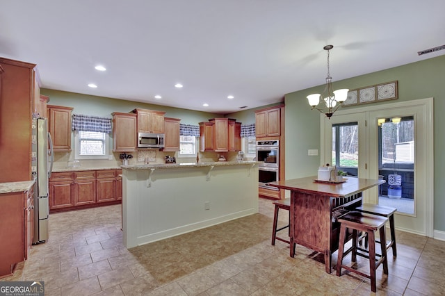 kitchen featuring an inviting chandelier, tasteful backsplash, a kitchen island, a kitchen bar, and stainless steel appliances