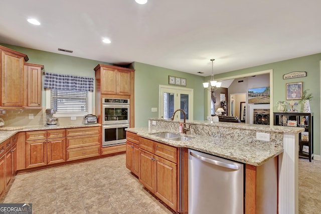 kitchen with hanging light fixtures, sink, a fireplace, appliances with stainless steel finishes, and a notable chandelier