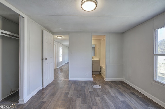 unfurnished bedroom with dark hardwood / wood-style flooring, multiple windows, connected bathroom, and a closet