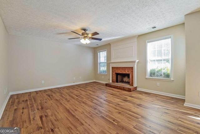 unfurnished living room featuring a textured ceiling, ceiling fan, light hardwood / wood-style floors, and a fireplace