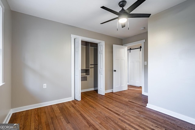 unfurnished bedroom with a barn door, ceiling fan, and wood-type flooring