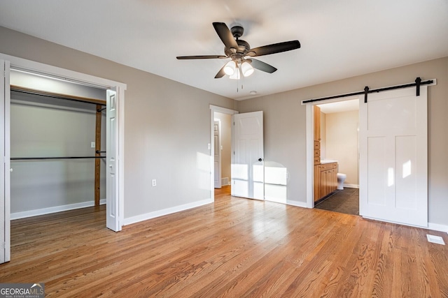 unfurnished bedroom with ceiling fan, a barn door, ensuite bathroom, light hardwood / wood-style floors, and a closet