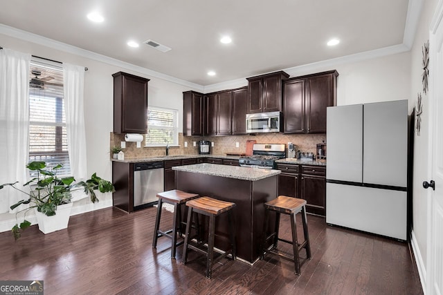 kitchen with appliances with stainless steel finishes, dark hardwood / wood-style flooring, a breakfast bar, sink, and a kitchen island