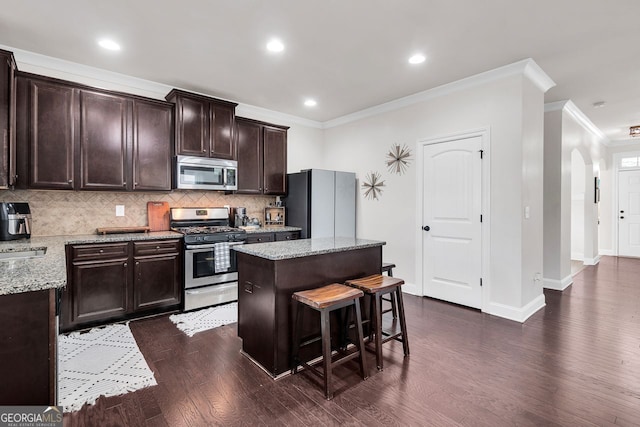 kitchen featuring appliances with stainless steel finishes, light stone counters, crown molding, a center island, and dark hardwood / wood-style floors