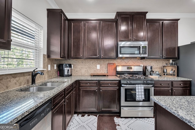 kitchen with appliances with stainless steel finishes, light stone counters, ornamental molding, dark brown cabinets, and sink