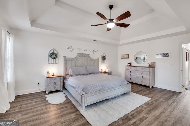 bedroom featuring dark hardwood / wood-style flooring, a tray ceiling, and ceiling fan