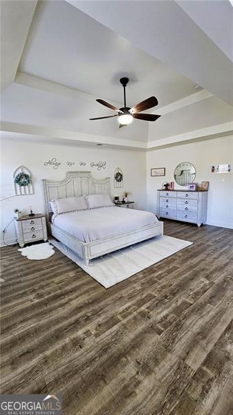 bedroom featuring a raised ceiling, ceiling fan, and dark wood-type flooring