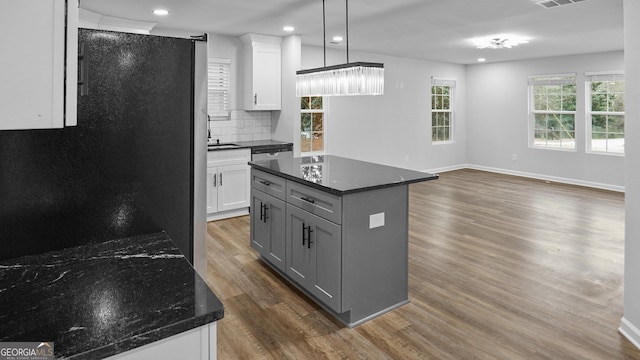 kitchen with decorative backsplash, dark hardwood / wood-style flooring, dark stone counters, a center island, and hanging light fixtures