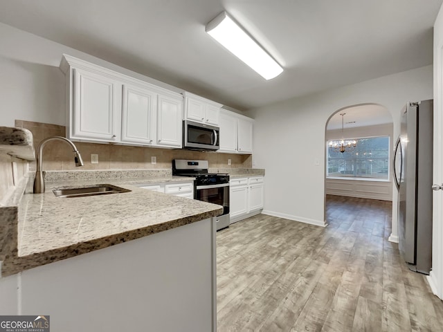 kitchen featuring light stone countertops, stainless steel appliances, sink, an inviting chandelier, and white cabinetry