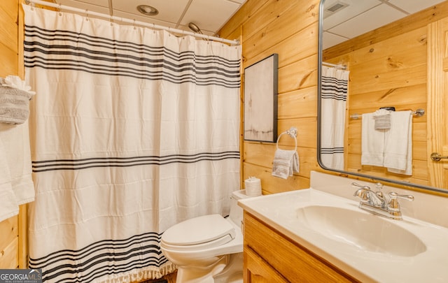 bathroom featuring a paneled ceiling, wooden walls, vanity, and toilet