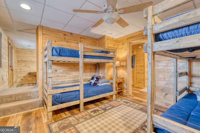 bedroom featuring wood-type flooring, a paneled ceiling, ceiling fan, and wood walls