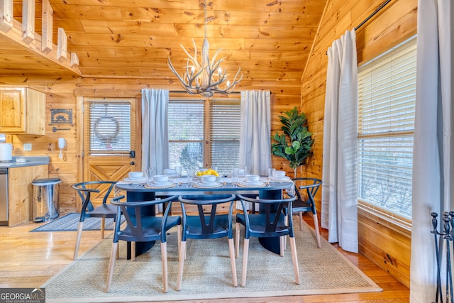 dining space featuring vaulted ceiling, light hardwood / wood-style floors, an inviting chandelier, and wooden walls