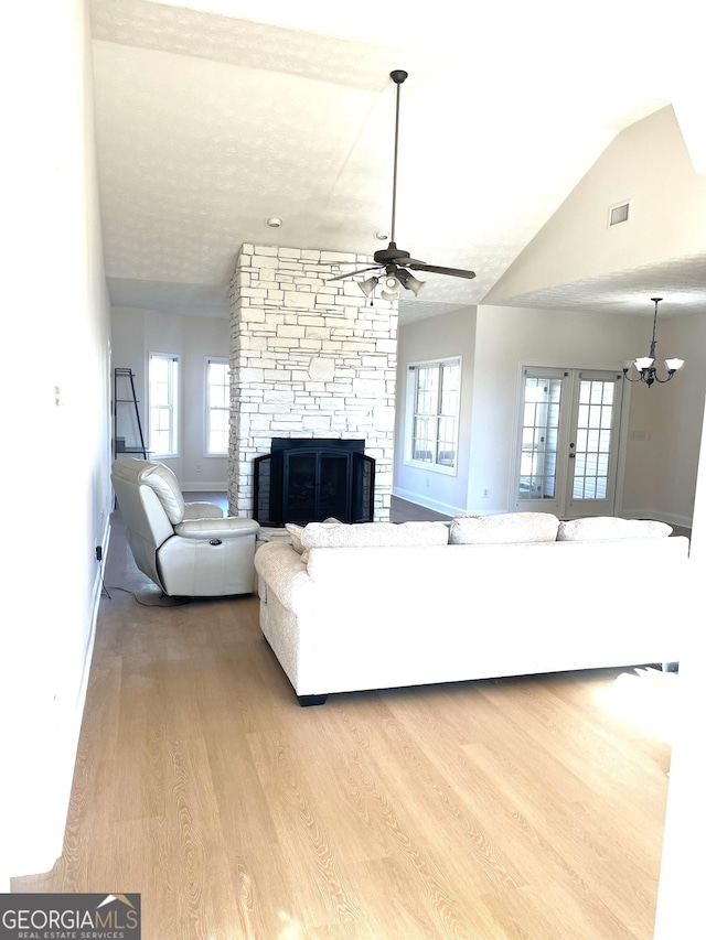 living room featuring ceiling fan with notable chandelier, a stone fireplace, lofted ceiling, and light hardwood / wood-style flooring