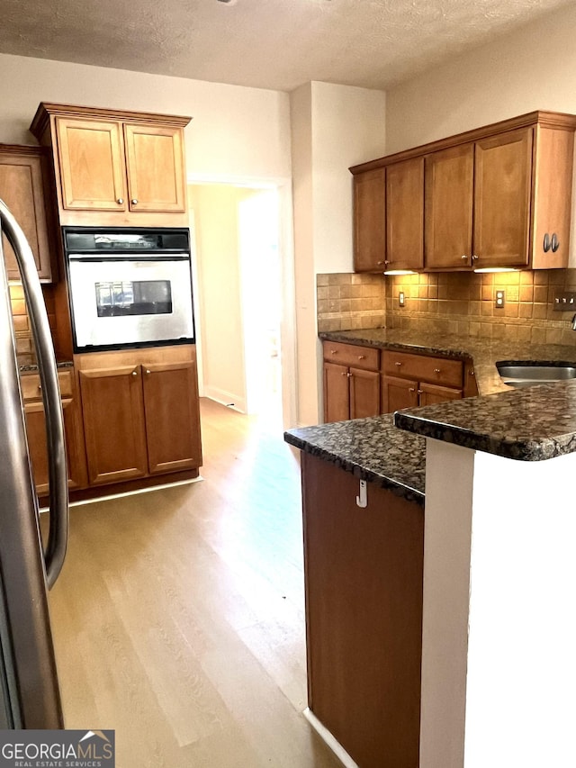 kitchen with sink, stainless steel appliances, light hardwood / wood-style flooring, dark stone counters, and decorative backsplash