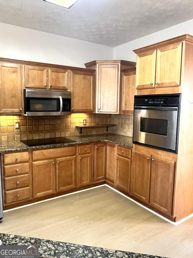 kitchen featuring stainless steel appliances, tasteful backsplash, dark stone countertops, a textured ceiling, and light wood-type flooring