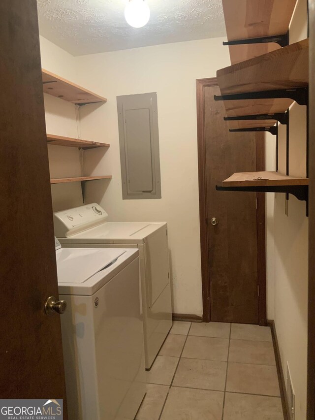 laundry area featuring light tile patterned floors, a textured ceiling, electric panel, and washing machine and clothes dryer