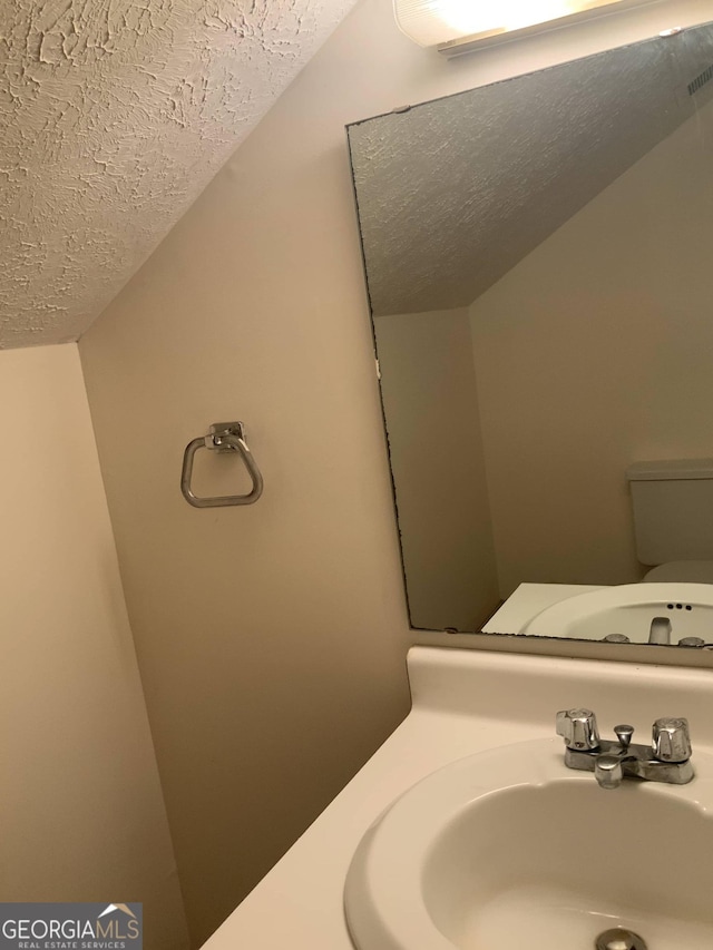 bathroom with a textured ceiling, toilet, and sink