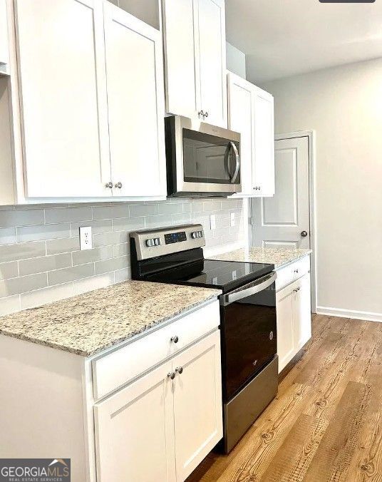 kitchen with white cabinetry, tasteful backsplash, light stone counters, light hardwood / wood-style floors, and appliances with stainless steel finishes