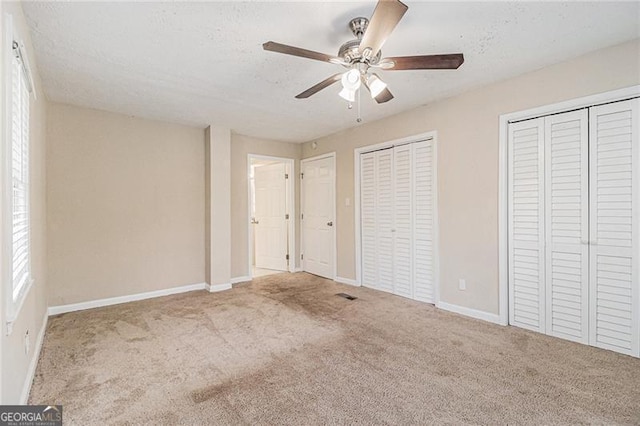 unfurnished bedroom featuring multiple closets, ceiling fan, light carpet, and a textured ceiling