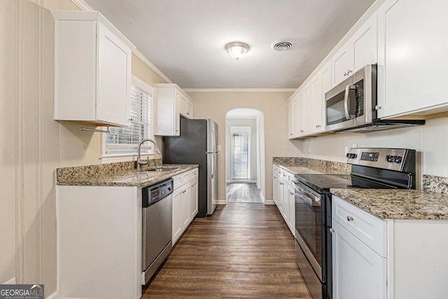 kitchen with light stone countertops, appliances with stainless steel finishes, ornamental molding, sink, and white cabinetry