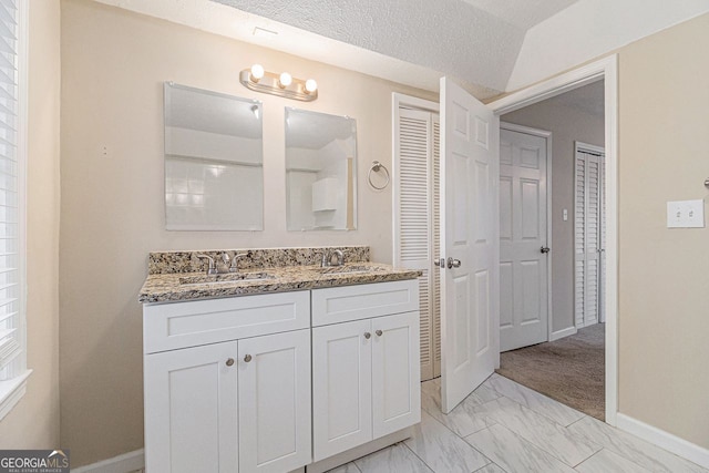 bathroom with vaulted ceiling, vanity, and a textured ceiling