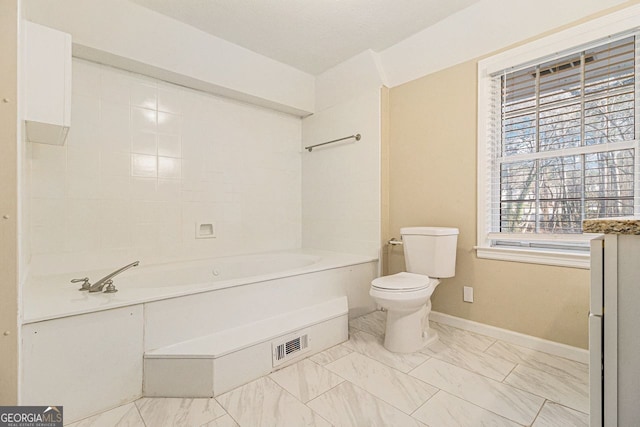 bathroom with a tub to relax in and toilet