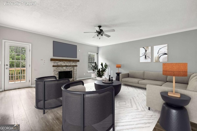 living room with a stone fireplace, crown molding, ceiling fan, and a textured ceiling