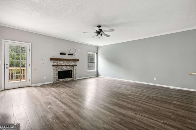 unfurnished living room with ceiling fan, dark wood-type flooring, a stone fireplace, crown molding, and a textured ceiling