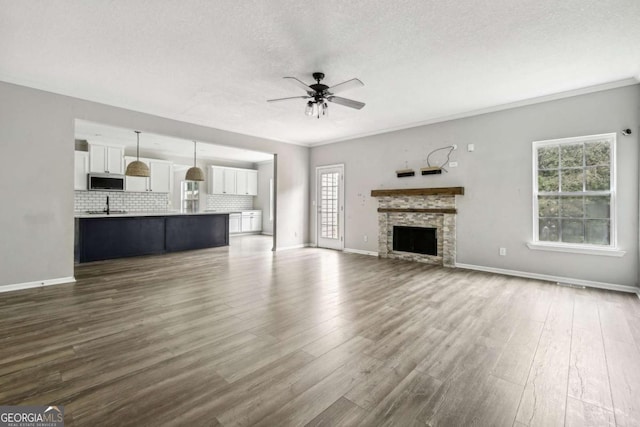 unfurnished living room featuring ceiling fan, sink, a stone fireplace, dark hardwood / wood-style floors, and crown molding