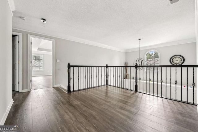 spare room featuring a textured ceiling, dark hardwood / wood-style floors, crown molding, and a notable chandelier