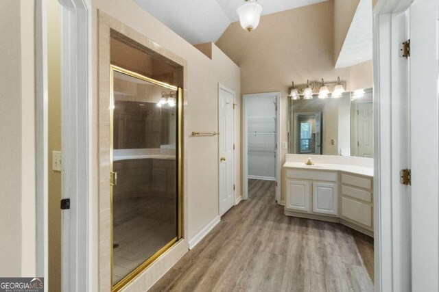 bathroom with a shower with door, vanity, vaulted ceiling, and hardwood / wood-style flooring