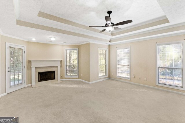 unfurnished living room featuring a raised ceiling, ceiling fan, ornamental molding, and a premium fireplace