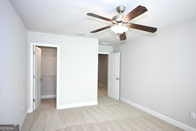 unfurnished bedroom featuring a walk in closet, ceiling fan, a closet, and light colored carpet