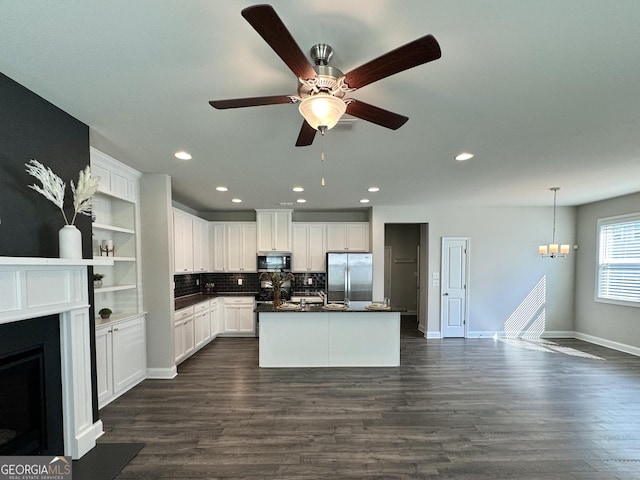 kitchen featuring dark wood-type flooring, white cabinets, a center island with sink, appliances with stainless steel finishes, and decorative light fixtures