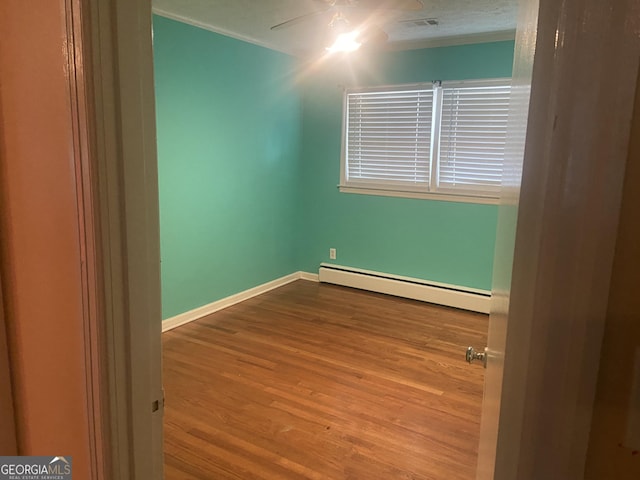 empty room with ceiling fan, hardwood / wood-style floors, and a baseboard heating unit