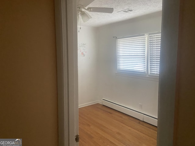 spare room with ceiling fan, baseboard heating, a textured ceiling, and light hardwood / wood-style flooring