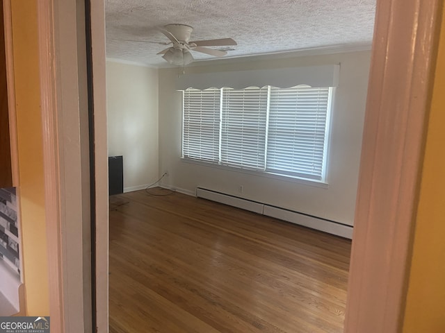 empty room with a baseboard heating unit, ceiling fan, a textured ceiling, and wood-type flooring