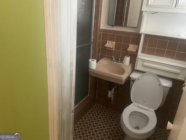 bathroom with a shower with shower door, tile walls, sink, and toilet