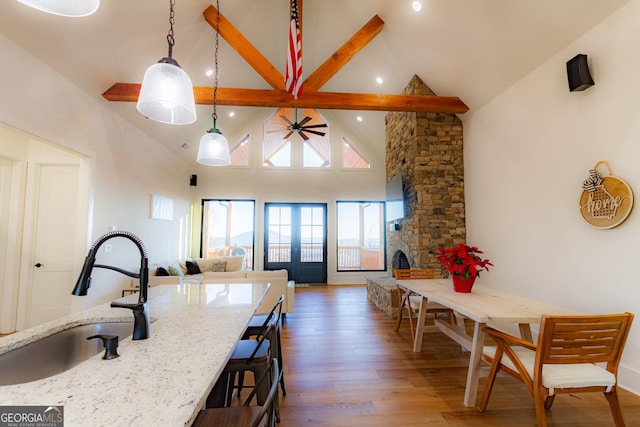 kitchen with light stone countertops, sink, decorative light fixtures, high vaulted ceiling, and beamed ceiling