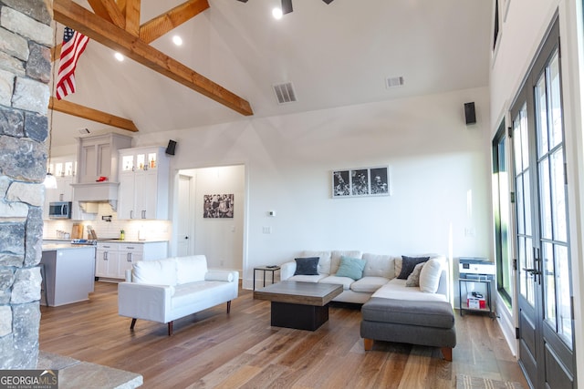 living room featuring beamed ceiling, french doors, light hardwood / wood-style floors, and a wealth of natural light