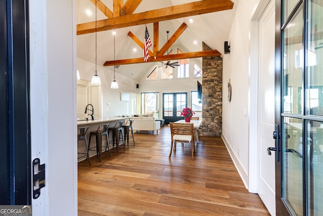 dining space with high vaulted ceiling, sink, ceiling fan, light wood-type flooring, and beam ceiling