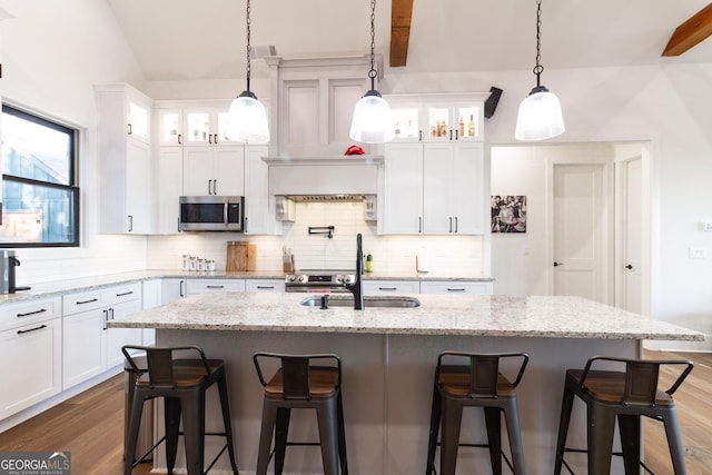 kitchen with white cabinets, beam ceiling, and an island with sink