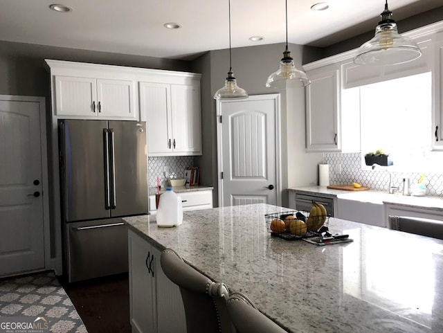 kitchen featuring white cabinetry, light stone counters, stainless steel refrigerator, backsplash, and hanging light fixtures