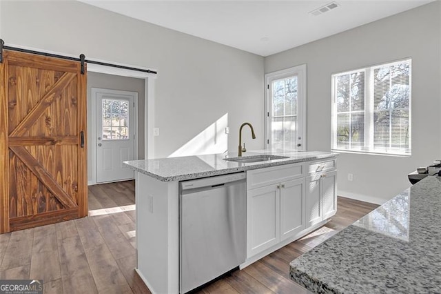 kitchen featuring stainless steel dishwasher, sink, a barn door, white cabinetry, and an island with sink