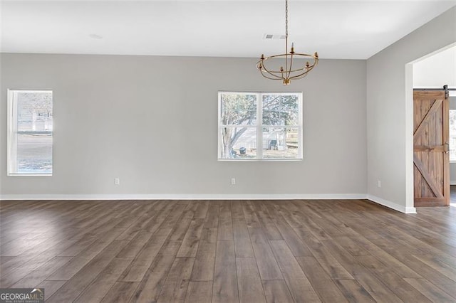 spare room with a notable chandelier, a barn door, and dark wood-type flooring