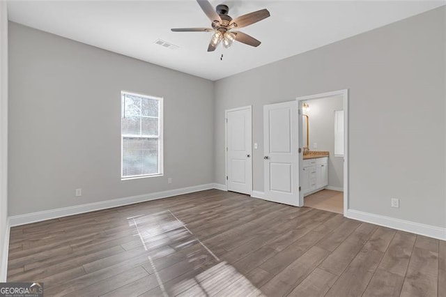 unfurnished bedroom featuring hardwood / wood-style flooring, ceiling fan, connected bathroom, and a closet