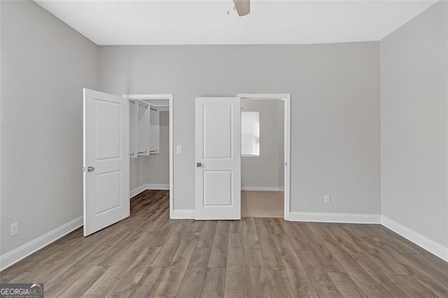 unfurnished bedroom featuring a spacious closet, a closet, ceiling fan, and light hardwood / wood-style floors