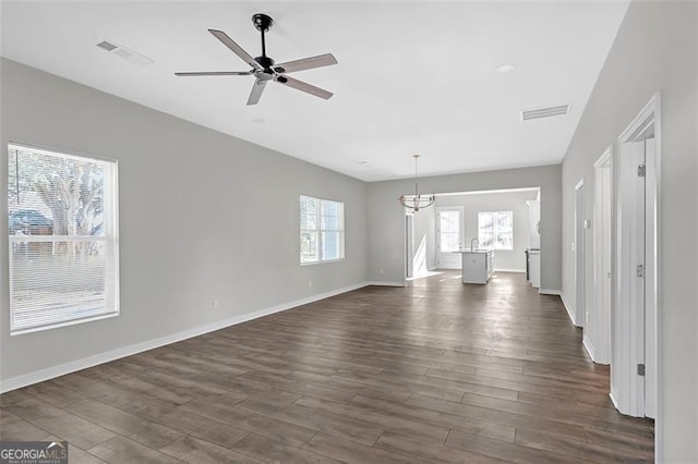 unfurnished living room featuring ceiling fan with notable chandelier and dark wood-type flooring