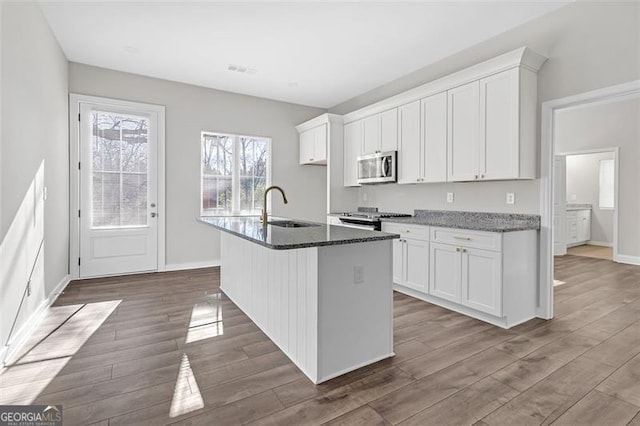 kitchen featuring sink, dark stone countertops, a center island with sink, white cabinets, and range